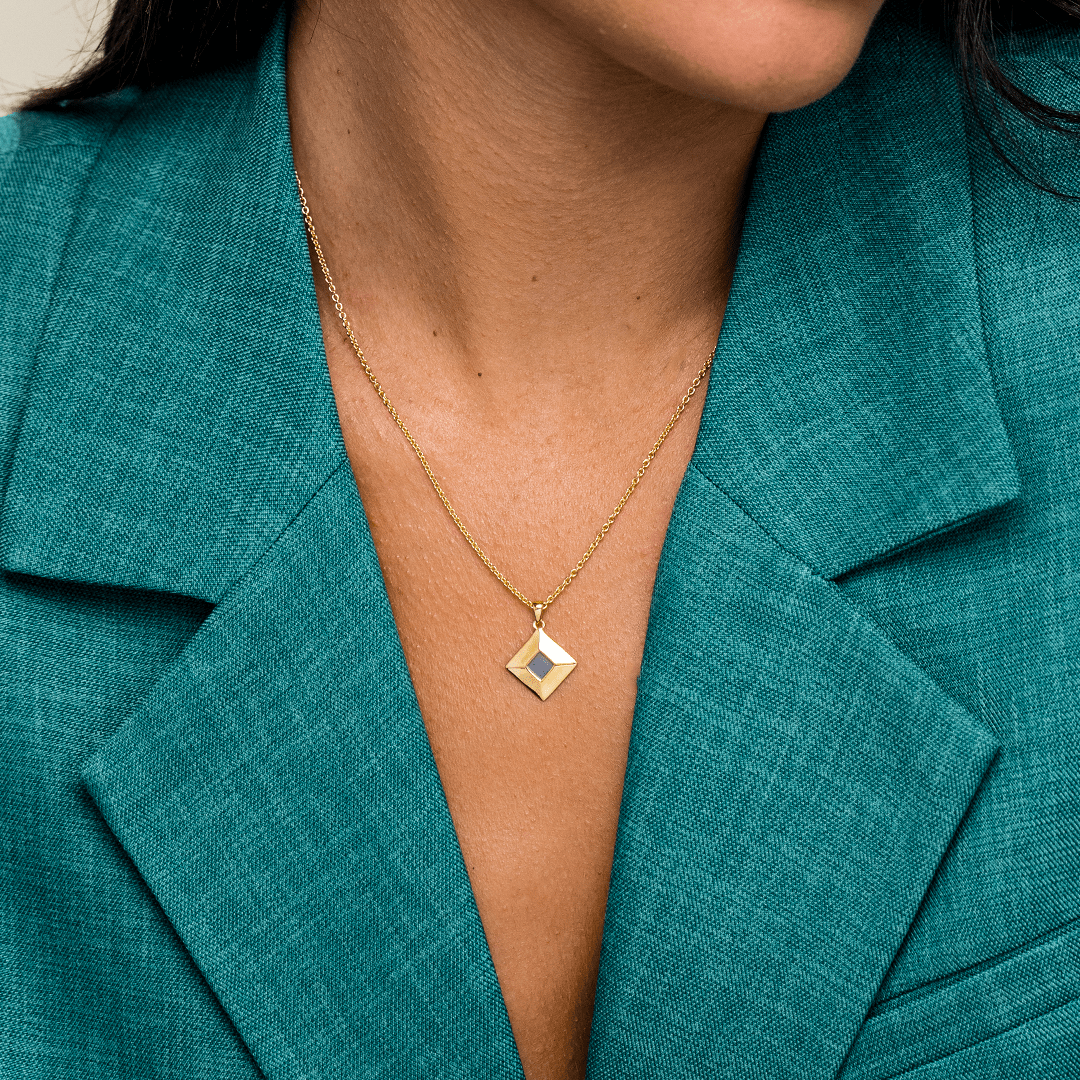 Person wearing a gold diamond-shaped necklace with a teal suit jacket.