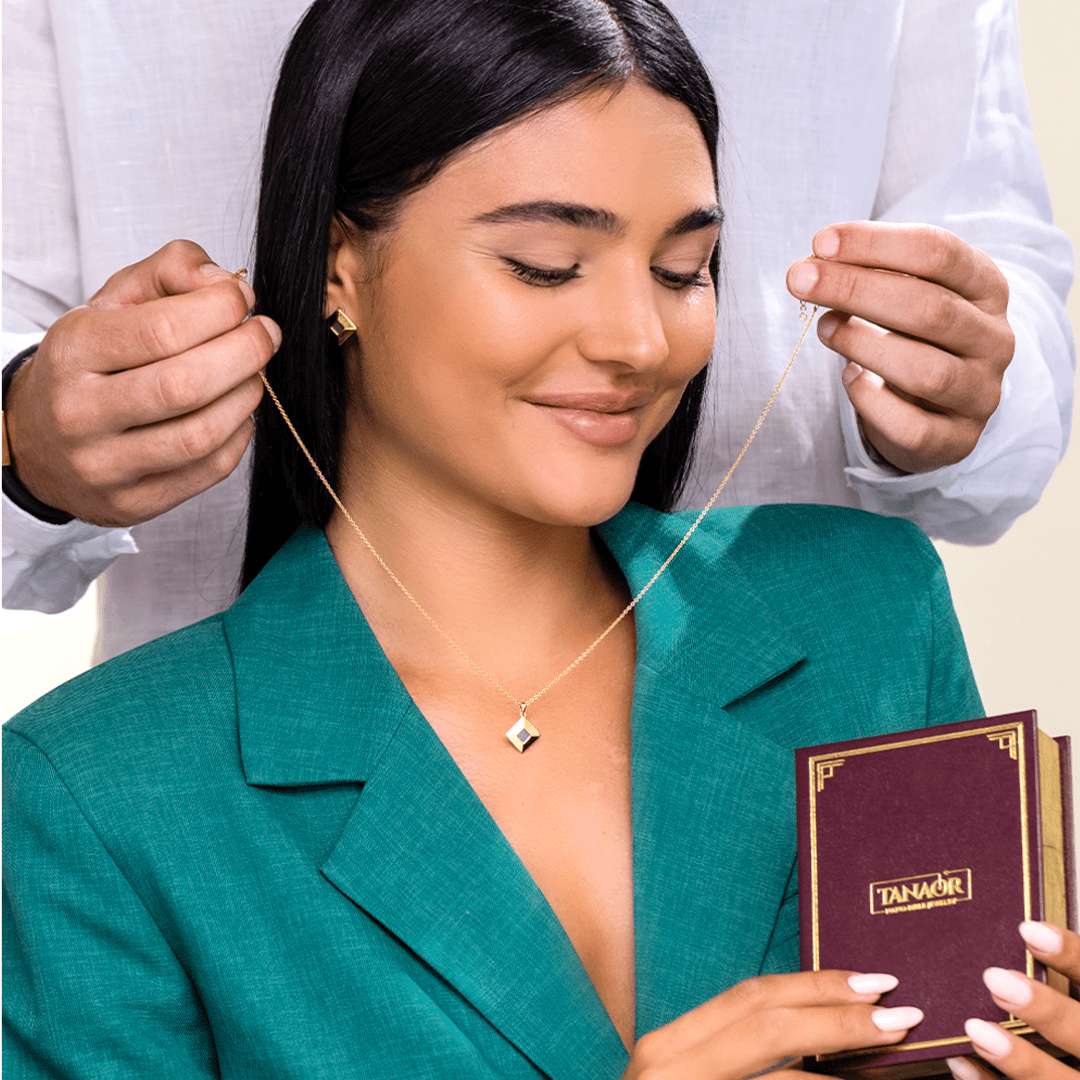 A woman receiving a gold necklace, smiling while holding a maroon box.